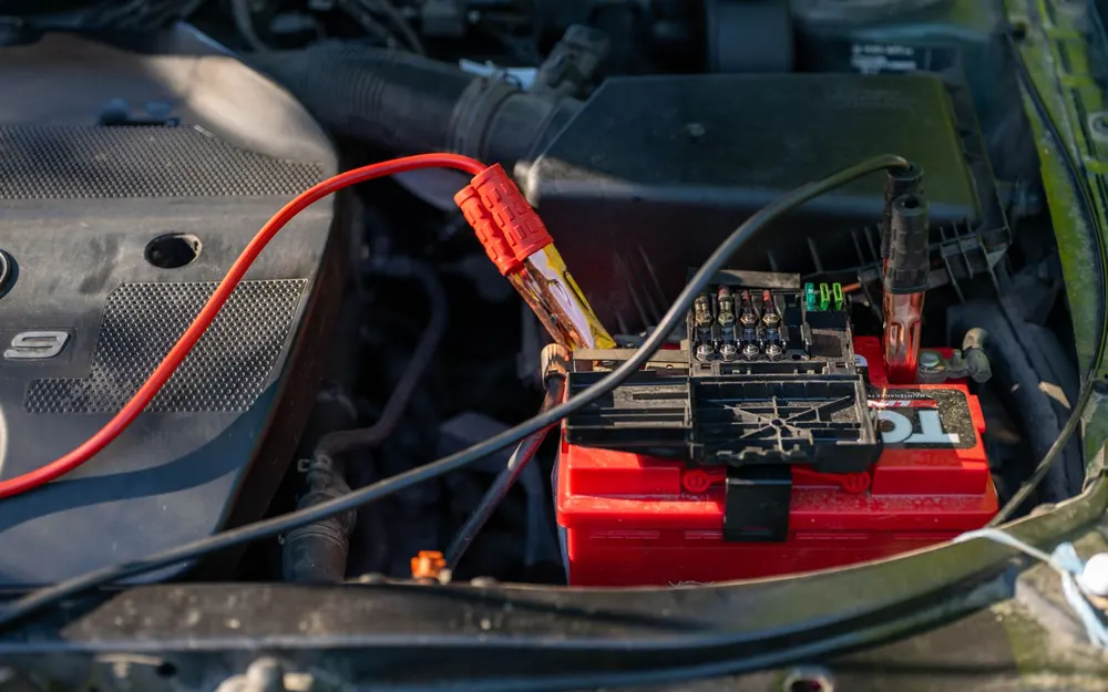 Batería de carro con cables de arranque conectados en el compartimento del motor